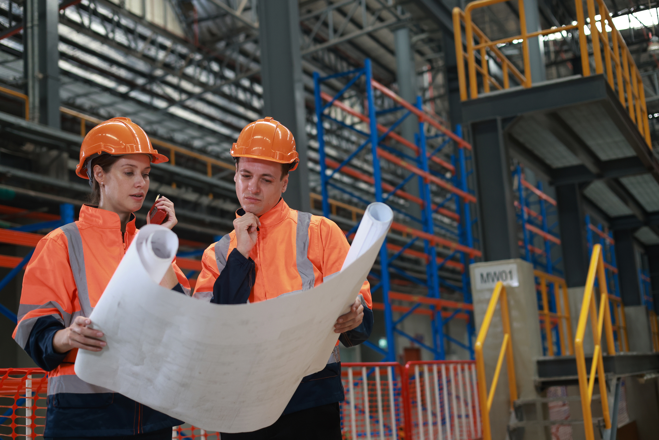 A female rail engineer used a walkie-talkie and discussed on blueprint with male technical at the rail station